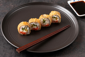 4 tempura rolls on a black plate with chopsticks and soy sauce