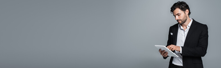 brunette businessman in black blazer using digital tablet isolated on grey, banner