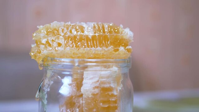 Drops of Honey Flows Spread a Thick Layer in a Glass Jar on a Bee Honeycomb. Yellow transparent, sticky flows drip over bee combs. Healing, organic, healthy, nutritious beekeeping product. Close up.
