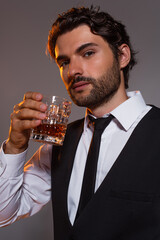 elegant man in white shirt and tie holding glass of whiskey and looking at camera isolated on grey
