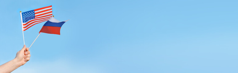 Flags of the USA, Russia in the hand of a man against the blue sky.Copy space fot text. Banner