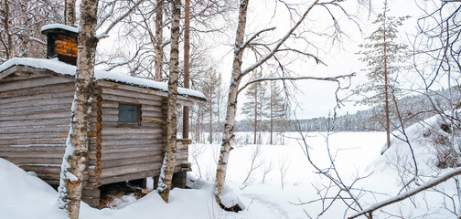 Naklejka premium Winter landscape, snow-covered forest, lake and log sauna. Oulanka National Park, Kuusamo, Finland, snowy forest.