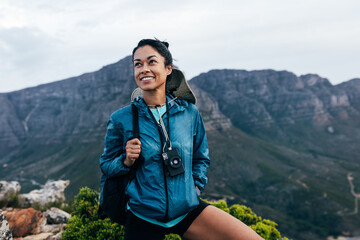 Portrait of a smiling woman relaxing during a mountain hike. Female with analog camera and backpack...