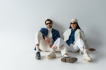 full length view of interracial couple in white and blue clothes sitting on grey