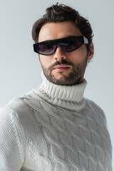 Obraz premium trendy man in white sweater and dark sunglasses looking at camera isolated on grey