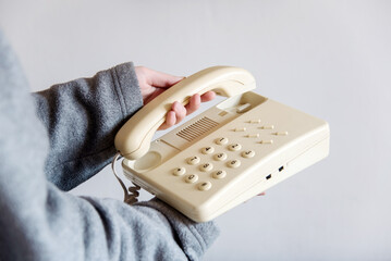 Detalle de una mano de mujer descolgando un teléfono blanco antiguo con cable. Mano sosteniendo el...