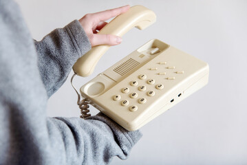 Detalle de una mano de mujer descolgando un teléfono blanco antiguo con cable. Mano sosteniendo el auricular de un teléfono fijo de casa u oficina. Concepto de atender una llamada telefónica.