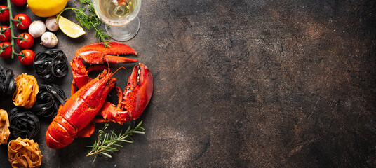 Cooked red lobters with ingredients for pasta and glass of whhite wine on dark background. Gourmet holidays food. Long banner with copy space
