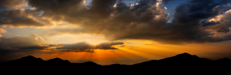 Panorama Dark cloud sunset over Dark mountain.Colorful sunrise with Clouds over hill.Sun hiding behind a cloud on the day sky.