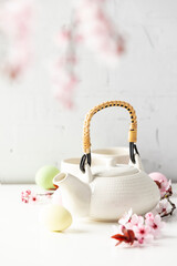 Easter composition with White ceramic teapot, Easter eggs and spring flowers on white table, selective focus
