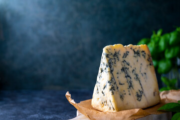Blue cheese, dor blue or roquefort mold cheese slice on cutting board with basil leaves, lifestyle...