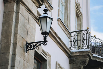 Old-fashioned street wall lamp made of black metal with snow. Gray facade of an old house with windows. Winter Lviv, Ukraine.
