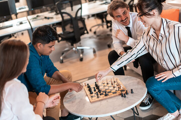 Multiethnic group of business people playing chess while having a break in relaxation area at modern startup office