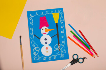 Children's Christmas paper crafts. Application of children's creativity. Kindergarten and craft school. On a beige background, a snowman made of colored paper.