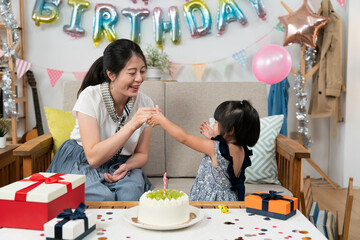 closeup shot of happy asian mother and baby girl having fun with party whistles on the birthday...