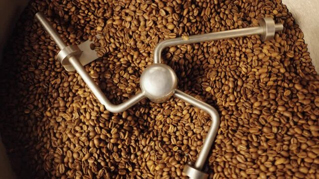 Top view of industrial mixing machine mixes roasted coffee beans in roaster, close up. Roasting process in coffee roasting machine in factory. Food and drink background for cafe. Slow motion.