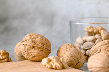 walnut lie on a wooden board. glass cup with nuts in the background. background gray