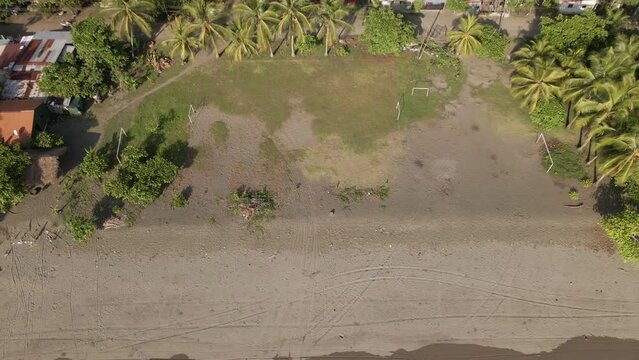 A rundown soccer field in El Cocal, Costa Rica bordering a tropical beach. Wide angle aerial reveal