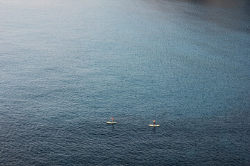 Two unrecognizable people stand up paddling on the ocean from high angle view with yellow boards