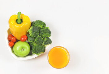 flat lay of vegetables  capsicum, broccoli tomatoes and green apple in heart shape plate  on white background with  a glass of orange  juice, copy space, healthy lifestyle and weight loss concept.