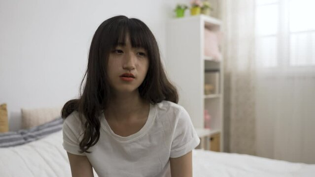 closeup view of a drowsy chinese girl nodding off in her bedroom and staring at the space blankly after waking up in the early morning at home.