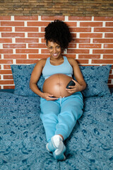 Happy and relaxed pregnant woman in her bed using a portable bluetooth speaker to play music for her baby.