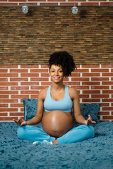 Healthy pregnant woman doing breathing and relaxation exercise sitting on her bed.