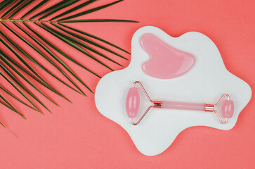 Facial skin care products. Quartz facial massager and gua sha massage scraper on a white podium.