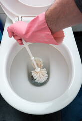 Male hand in latex glove using a toilet brush to scrub the WC bowl. Top view, no face