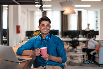 Casual business man taking break from the work using laptop while drinking tea in relaxation area of modern open plan startup office