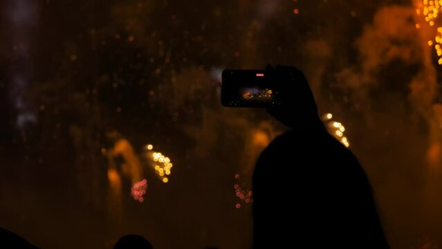 Slow motion: woman hands silhouette taking photo or recording video of colorful fireworks in dark sky with smartphone at night. Holiday, technology, abstract, entertainment and anniversary concept