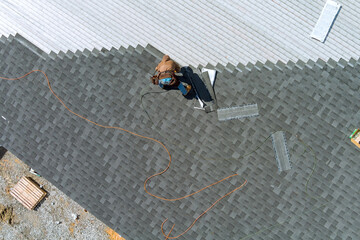 A asphalt shingles installation on the roof roofer is nailing asphalt shingles to roofing construction