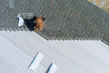 A worker installing shingles on the roof of a home © ungvar