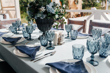 Blue glasses, plates and utensils on a festive table with flowers.