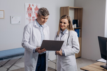 Two doctors talking about patients diagnosis using laptop to look at checkup results. Team of senior medical professionals having consultation.