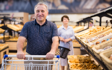 mature man choosing bread and baking in grocery section of supermarket