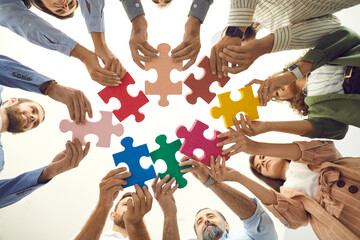 Creative business team trying to fit colorful jigsaw puzzle pieces together, low angle shot from below, bottom view. Group of happy people enjoying teamwork, finding solution, starting new enterprise - obrazy, fototapety, plakaty