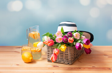 Colorful fresh tulips in wicker basket, hat and fresh lemonade on wooden table. Selective focus.