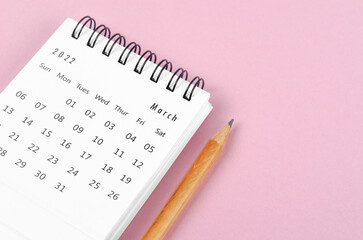 March 2022 desk calendar with wooden pencil on pink background.