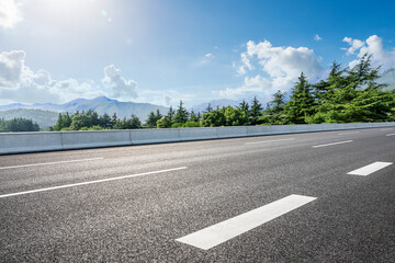 Country road and green forest with mountain scenery under blue sky
