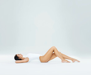 Obraz premium Young, fit and beautiful brunette woman in white swimsuit posing in studio. Concept of fitness, dieting and skin care.