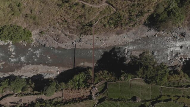metal wire suspension bridge spanning across a rocky mountain river in Kabayan Benguet Philippines bird's eye view top down wide angle aerial