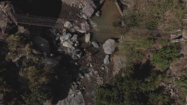 two people bathing under metal wire suspension bridge spanning across a rocky mountain river creek in Kabayan Benguet Philippines bird's eye view top down wide angle aerial