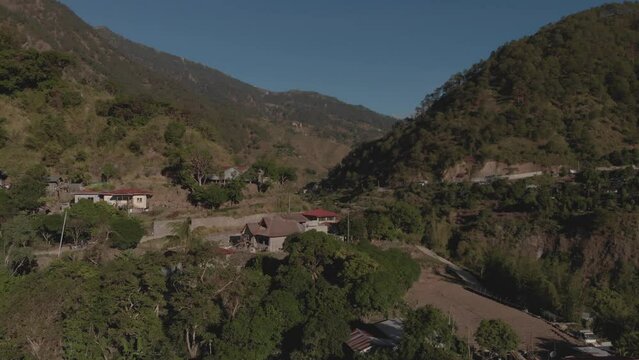 remote village town in mountainous tropical region Kabayan Benguet Philippines aerial fast approaching wide angle approaching house on edge of valley blue sky sunny day