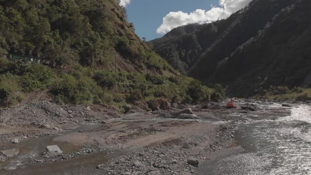 excavator digging rock out of river bed in mountainous region in Benguet Kabayan Philippines wide angle aerial approaching raw cement material mining