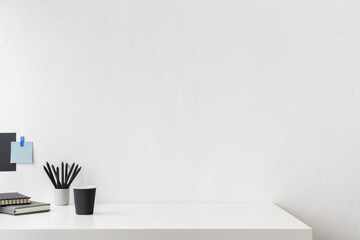 Front view white desk with supplies, coffee mug and copy space. Table at home office against white wall. Stylish minimalist workspace.	
