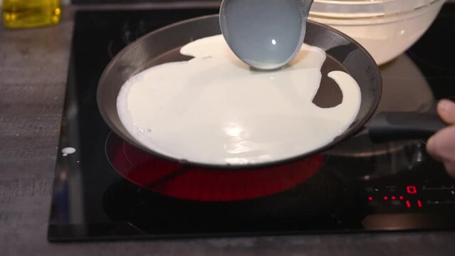 The woman pouring pancake batter into a frying pan. Crepes are fried in a pan. homemade Russian blini baking process. Cooking smoke goes up from pancake. close uo