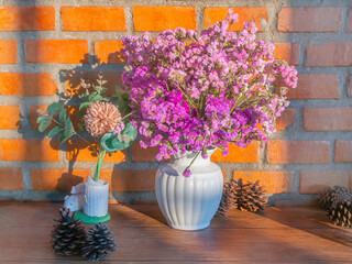 blossom pink and magenta flower in pot on wood table in front of orange brick wall, decoration with pine cones