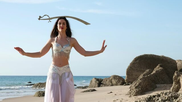 Woman dancing belly dance with sword barefoot on the beach. Oriental Beauty.
