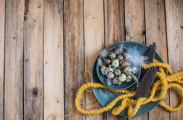 Dekoration Ostern mit Wachteleiern und Federn auf Teller, Tischdekoration im Frühling
